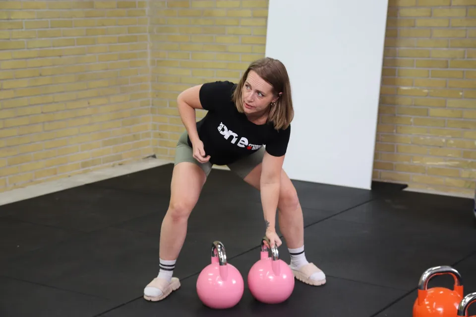 Kvinde laver styrketræning med kettlebells på gulvet hos Box One i Roskilde