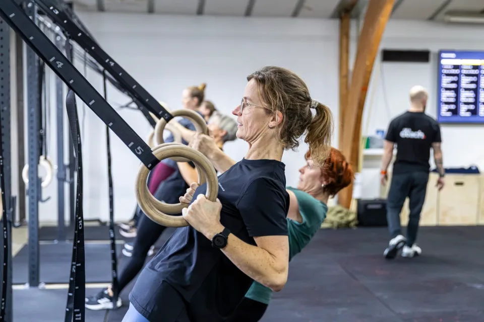 En kvinde træner i gymnastikringe sammen med andre medlemmer i Box One.