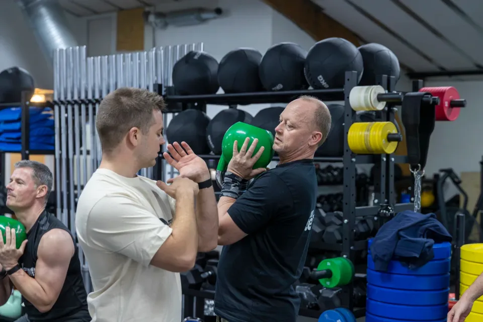 En coach guider et medlem, der træner med en grøn kettlebell.