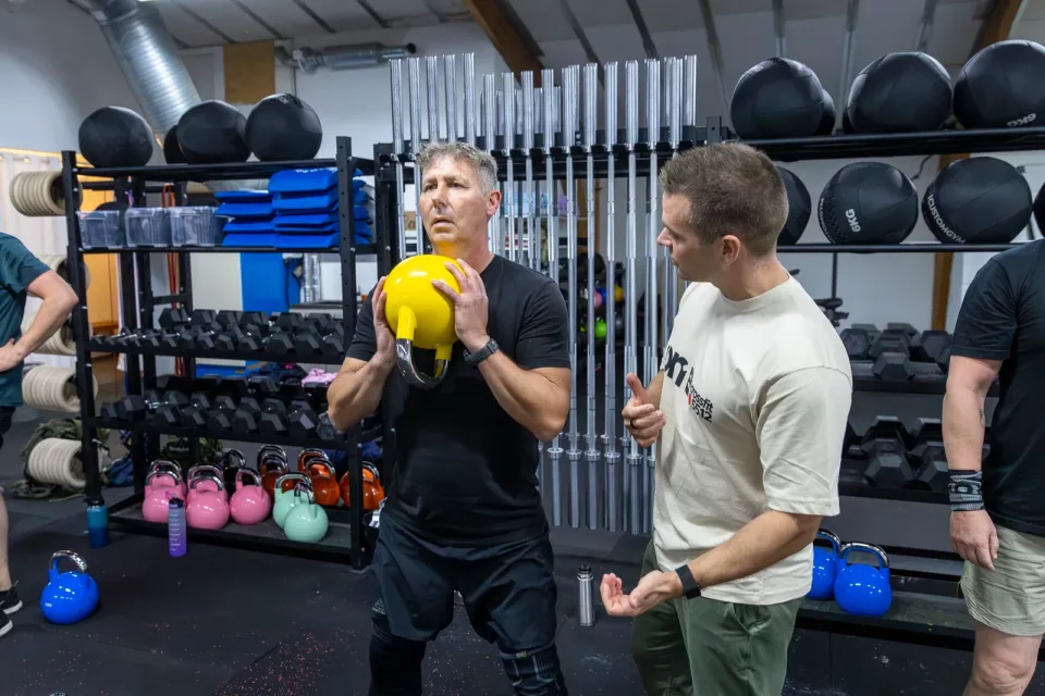 En coach guider et medlem, der træner med en gul kettlebell.