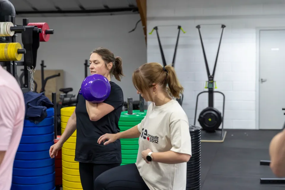 En kvinde træner med en lilla kettlebell, mens en coach følger med.